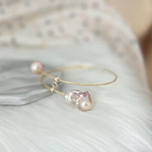 Peut inclure: Un bracelet jonc en or avec deux perles. La plus grosse perle est une perle baroque de forme irr&eacute;guli&egrave;re et de couleur rose. La plus petite perle est ronde et blanche.