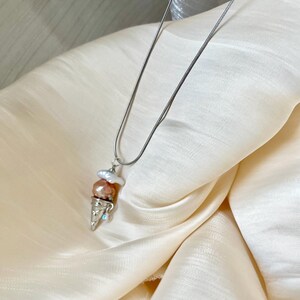 Peut inclure: Un collier en cha&icirc;ne argent&eacute;e avec un pendentif en forme de cornet de glace. Le cornet est rempli de trois boules de glace nacr&eacute;es dans des tons de rose et de blanc.
