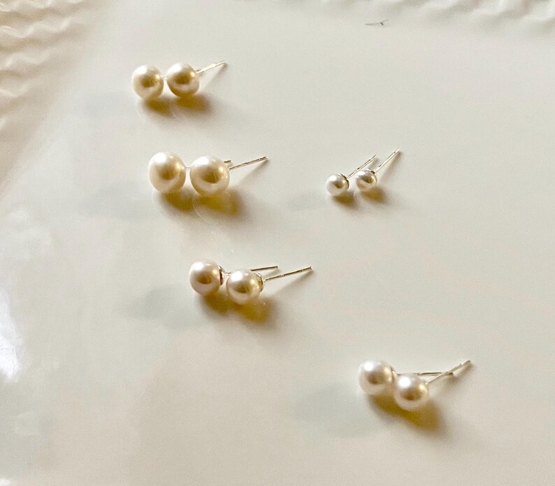 Peut inclure: Plusieurs paires de boucles d'oreilles en perles de diff&eacute;rentes tailles sont dispos&eacute;es sur une surface blanche. Les boucles d'oreilles ont des perles rondes classiques et des tiges en argent. Les perles sont de couleur cr&egrave;me.