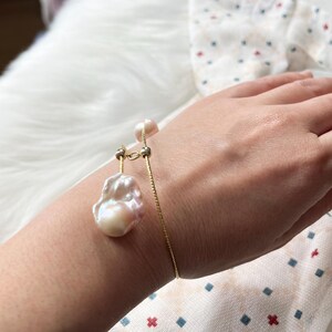 Peut inclure: Un bracelet en cha&icirc;ne dor&eacute;e avec un grand pendentif de perle irr&eacute;guli&egrave;re. La perle est de couleur blanc cass&eacute;.