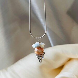 Peut inclure: Un collier en cha&icirc;ne argent avec un pendentif en forme de cornet de glace en perle et coquille blanche.