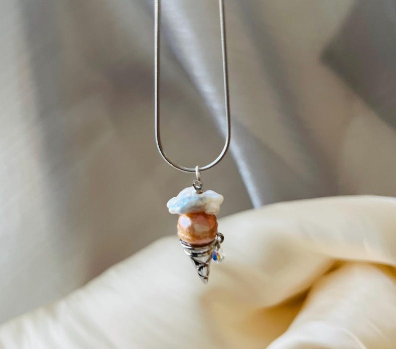 Peut inclure: Un collier en cha&icirc;ne argent avec un pendentif en forme de cornet de glace en perle et coquille blanche.