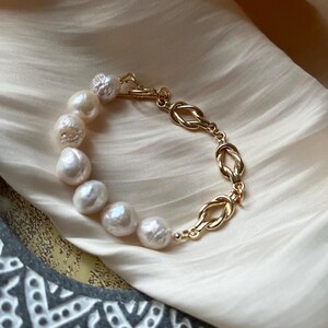 Puede incluir: Un brazalete de cadena dorada con un dise&ntilde;o anudado y una fila de perlas blancas.