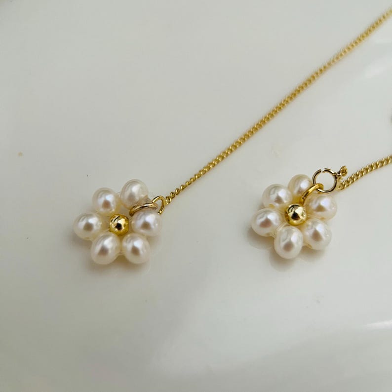 May include: A pair of gold chain earrings with pearl flower charms. Each flower charm is made of six white pearls arranged in a circular pattern.