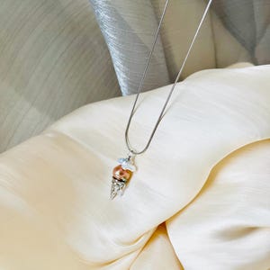 Peut inclure: Un collier en cha&icirc;ne argent avec un pendentif en forme de cornet de glace. Le cornet est en argent et a trois boules de fausses perles dans des tons de blanc et de p&ecirc;che.