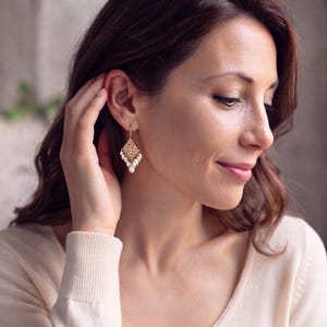 Peut inclure: Une boucle d'oreille pendante dor&eacute;e compos&eacute;e d'une pi&egrave;ce en m&eacute;tal filigran&eacute; en forme de losange suspendue &agrave; un crochet, orn&eacute;e d'une grappe de petites perles blanches en forme de goutte fix&eacute;es au bas de la structure.