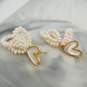 May include: A pair of gold earrings with a heart-shaped pendant made of white mother of pearl. The earrings are made of small white pearls.