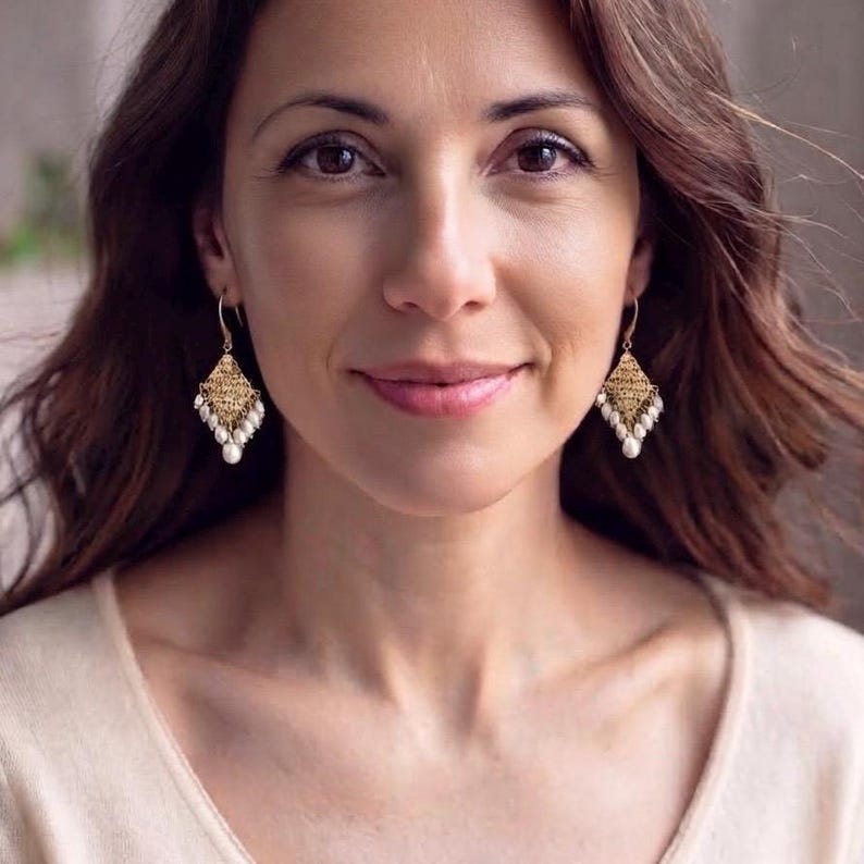 Peut inclure: Boucles d'oreilles pendantes dor&eacute;es avec un motif en m&eacute;tal filigran&eacute; en forme de losange. Le bord inf&eacute;rieur de chaque boucle est orn&eacute; d'une s&eacute;rie de petites perles blanches en forme de goutte qui pendent librement du m&eacute;tal dor&eacute;.