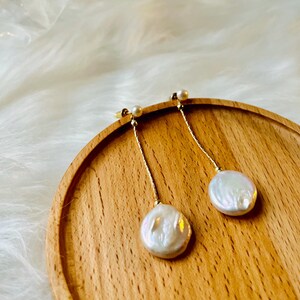 May include: A pair of gold dangle earrings with white pearl drops. The earrings are on a wooden surface.