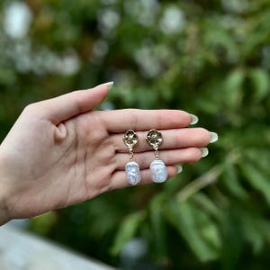 Puede incluir: Pendientes de oro con un dise&ntilde;o floral texturizado y una gran perla blanca.