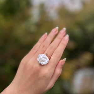 May include: A white pearl ring with a rose-shaped design. The ring is made of gold and has a simple band.