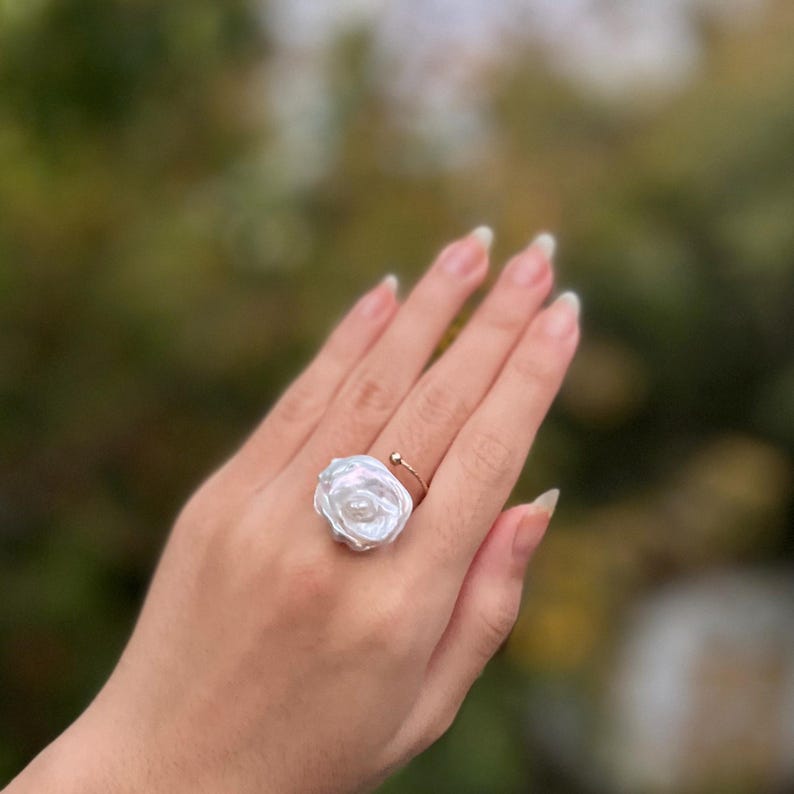 May include: A white pearl ring with a rose-shaped design. The ring is made of gold and has a simple band.