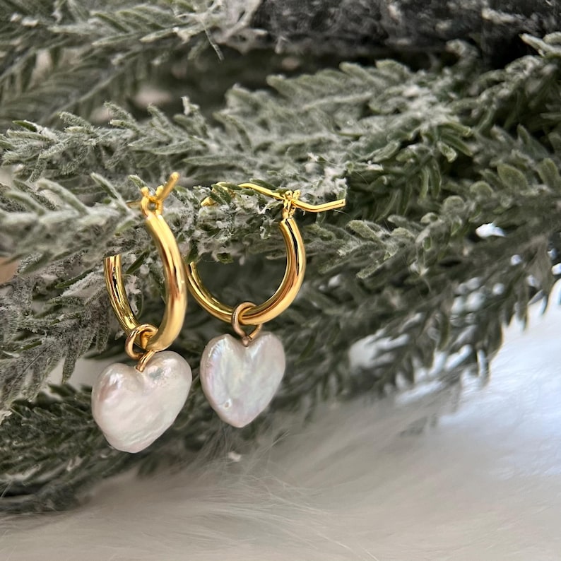 Op de afbeelding: Gouden creolen met een witte parelhart-hanger aan elke creool.