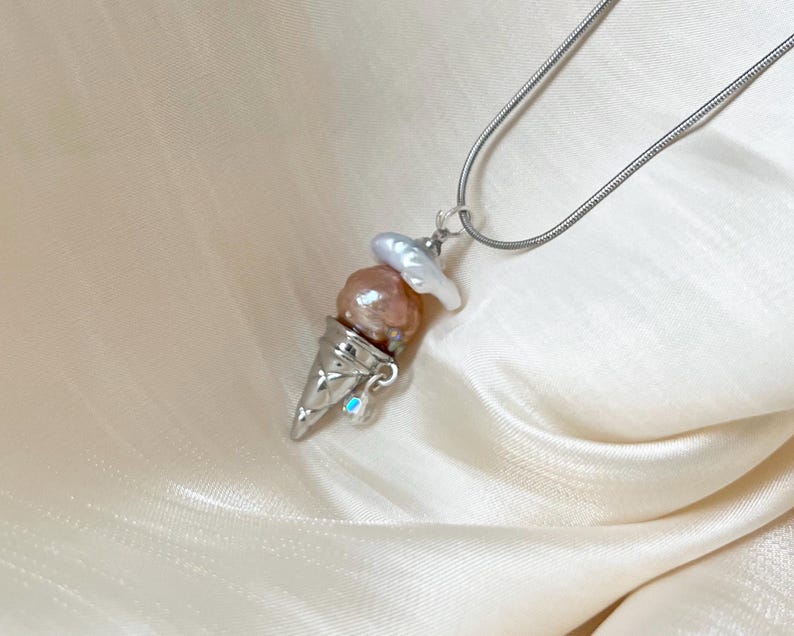 Peut inclure: Un collier en cha&icirc;ne argent avec un pendentif en forme de cornet de glace. Le cornet est rempli de trois perles roses et blanches.