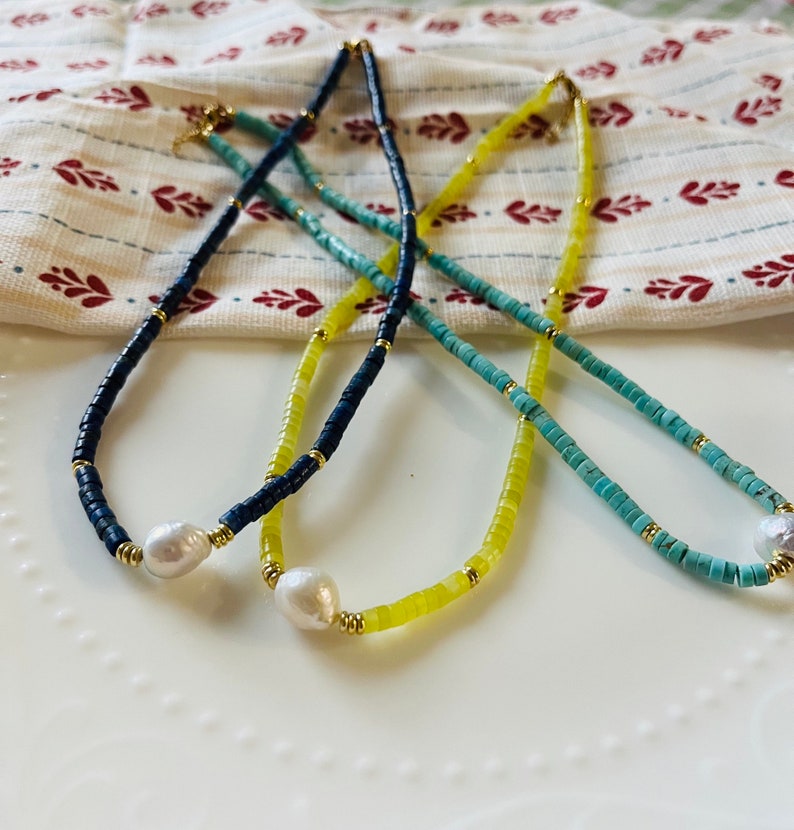 May include: Three necklaces with different colored beads and a pearl pendant. The necklaces are blue, yellow, and turquoise.