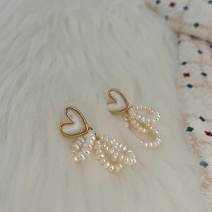 May include: A pair of gold heart-shaped earrings with white pearl drop accents.