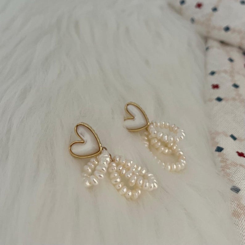 May include: A pair of gold heart-shaped earrings with white pearl drop accents.