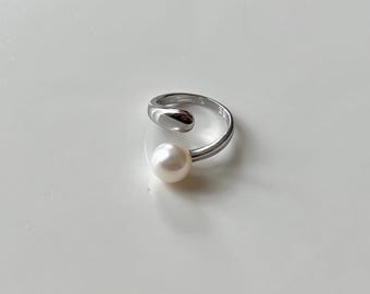 May include: A silver ring with a pearl accent. The ring is open and has a curved design.