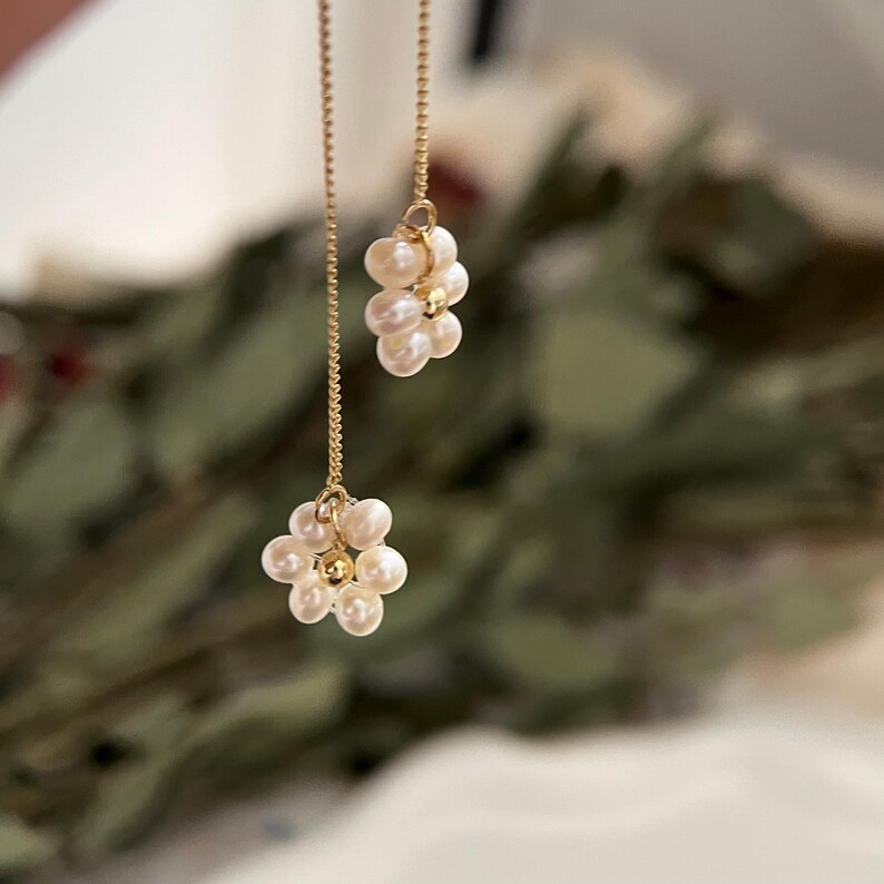 May include: A pair of gold chain earrings with pearl flower accents. Each earring features a cluster of small white pearls arranged in a flower shape.