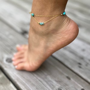 May include: A gold anklet with turquoise beads. The anklet is layered with two chains.