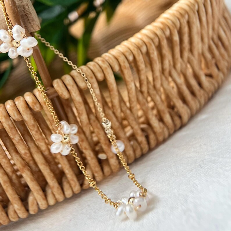 May include: A delicate gold chain necklace with three clusters of small white pearls arranged in flower shapes.