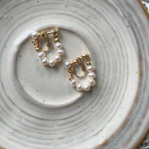 May include: A pair of gold-toned clip-on earrings with a cluster of white pearls in a circular design.