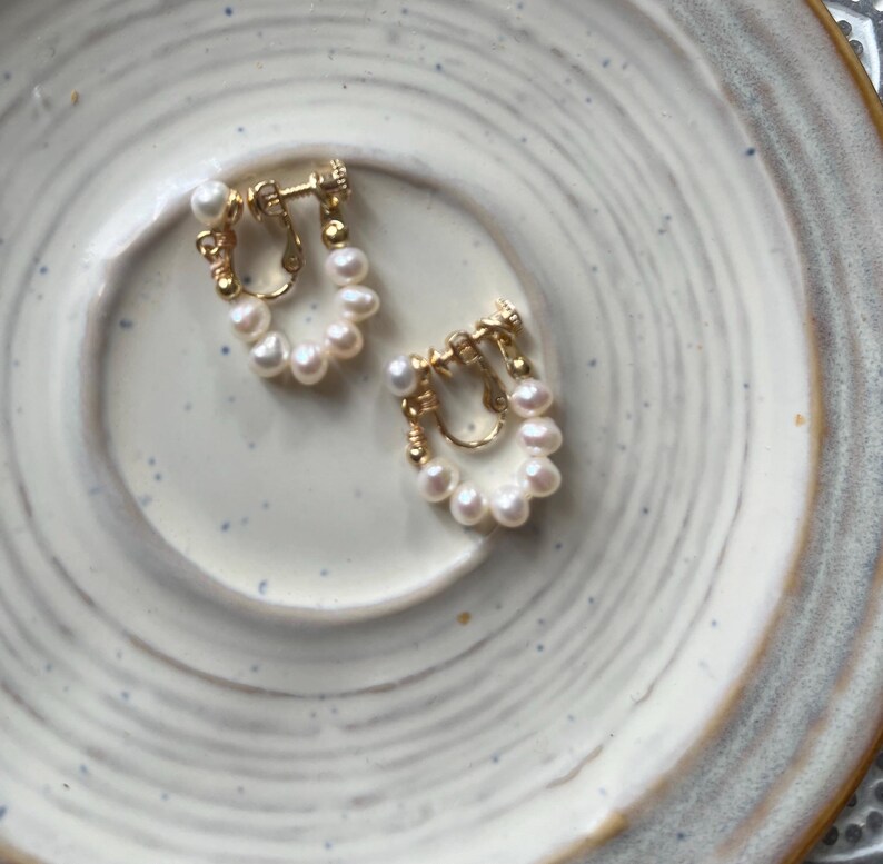 May include: A pair of gold-toned clip-on earrings with a cluster of white pearls in a circular design.