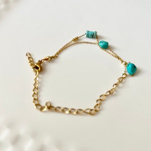 May include: A gold chain bracelet with turquoise beads. The bracelet has a lobster clasp closure.