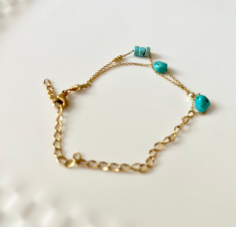 May include: A gold chain bracelet with turquoise beads. The bracelet has a lobster clasp closure.