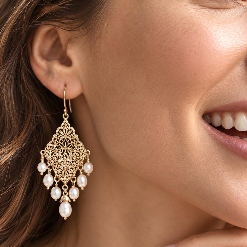 Peut inclure: Une boucle d'oreille pendante dor&eacute;e avec une pi&egrave;ce centrale en m&eacute;tal filigran&eacute; en forme de losange. Sept petites perles blanches rondes sont suspendues au bas du filigrane dans une disposition en cascade.