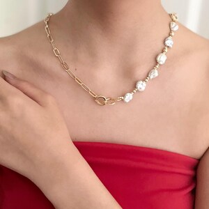 Peut inclure: Collier dor&eacute; avec un motif de cha&icirc;ne et une rang&eacute;e de perles blanches irr&eacute;guli&egrave;res. Le collier est port&eacute; sur un haut rouge, cr&eacute;ant un contraste saisissant. Le bijou est un accessoire &eacute;l&eacute;gant.