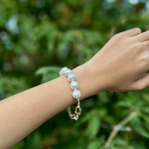 Puede incluir: Un brazalete de perlas blancas con cierre de cadena dorada. Las perlas son grandes e irregulares.