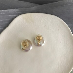 May include: A pair of white pearl earrings with gold wire accents. The earrings are round and have a slightly irregular shape. The gold wire is coiled into a spiral shape.