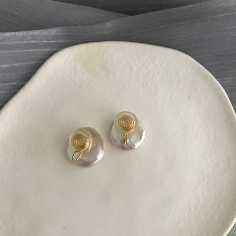 May include: A pair of white pearl earrings with gold wire accents. The earrings are round and have a slightly irregular shape. The gold wire is coiled into a spiral shape.