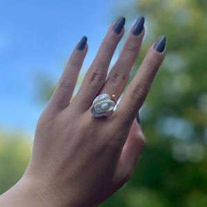 May include: A white pearl ring with a gold band. The ring is shaped like a flower with multiple layers of pearls.