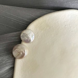 May include: Two white pearl earrings on a white ceramic surface.