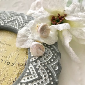 May include: A pair of pearl stud earrings with gold posts. The pearls are white and iridescent.