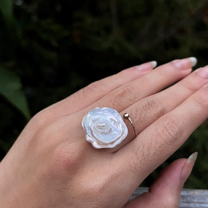 May include: A white pearl ring with a delicate gold band. The pearl is shaped like a flower with multiple layers.