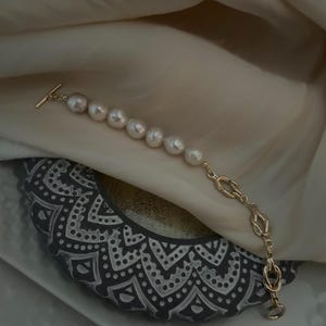 Puede incluir: Un brazalete de cadena dorada con una serie de perlas blancas grandes. La cadena tiene un dise&ntilde;o de nudo.