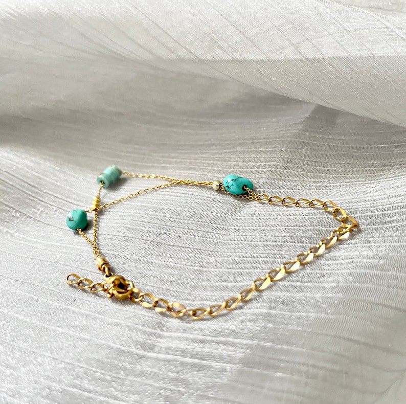 May include: A gold chain bracelet with turquoise beads. The bracelet has a lobster clasp closure.