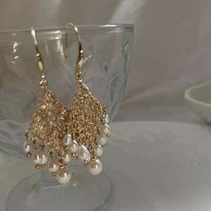 Peut inclure: Une paire de boucles d'oreilles pendantes dor&eacute;es compos&eacute;es d'un maillage m&eacute;tallique filigrane d&eacute;licat et complexe en forme de triangle, orn&eacute; de multiples petites perles d'eau douce blanches et rondes suspendues aux crochets.