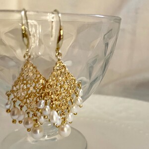 Peut inclure: Une paire de boucles d'oreilles pendantes dor&eacute;es avec un motif en filigrane en forme de losange. Chaque boucle est orn&eacute;e de plusieurs petites perles d'eau douce blanches de forme irr&eacute;guli&egrave;re suspendues par de fins maillons dor&eacute;s.