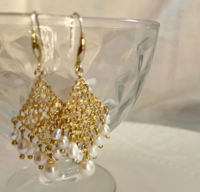 Peut inclure: Une paire de boucles d'oreilles pendantes dor&eacute;es avec un motif en filigrane en forme de losange. Chaque boucle est orn&eacute;e de plusieurs petites perles d'eau douce blanches de forme irr&eacute;guli&egrave;re suspendues par de fins maillons dor&eacute;s.