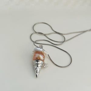 Peut inclure: Un collier en cha&icirc;ne argent avec un pendentif en forme de cornet de glace. Le cornet est rempli de trois couches de perles roses et blanches.