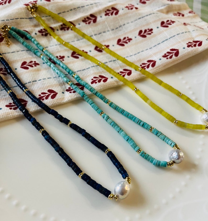 May include: Three necklaces with different colored beads and a pearl pendant. The necklaces are blue, turquoise, and yellow.