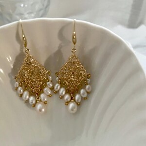 Peut inclure: Une paire de boucles d'oreilles pendantes dor&eacute;es avec un &eacute;l&eacute;ment en m&eacute;tal filigran&eacute; en forme de losange. Chaque boucle est orn&eacute;e de plusieurs petites perles d'eau douce blanches de forme ovale suspendues &agrave; la base.