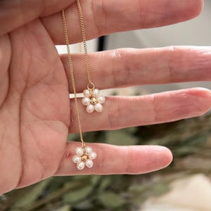 May include: A delicate gold chain necklace with two pearl flower charms. Each flower charm is made of small white pearls arranged in a circular pattern.