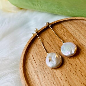 May include: A pair of gold dangle earrings with white pearl drops. The pearls are round and have an iridescent sheen.