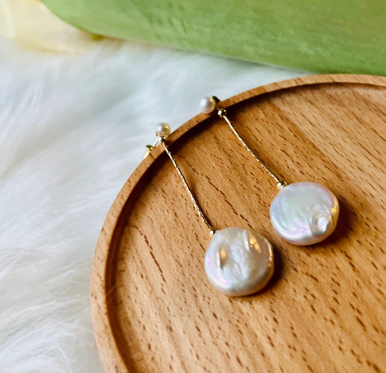 May include: A pair of gold dangle earrings with white pearl drops. The pearls are round and have an iridescent sheen.