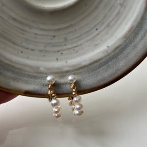 May include: A pair of gold clip-on earrings with a cluster of white pearls dangling from each.